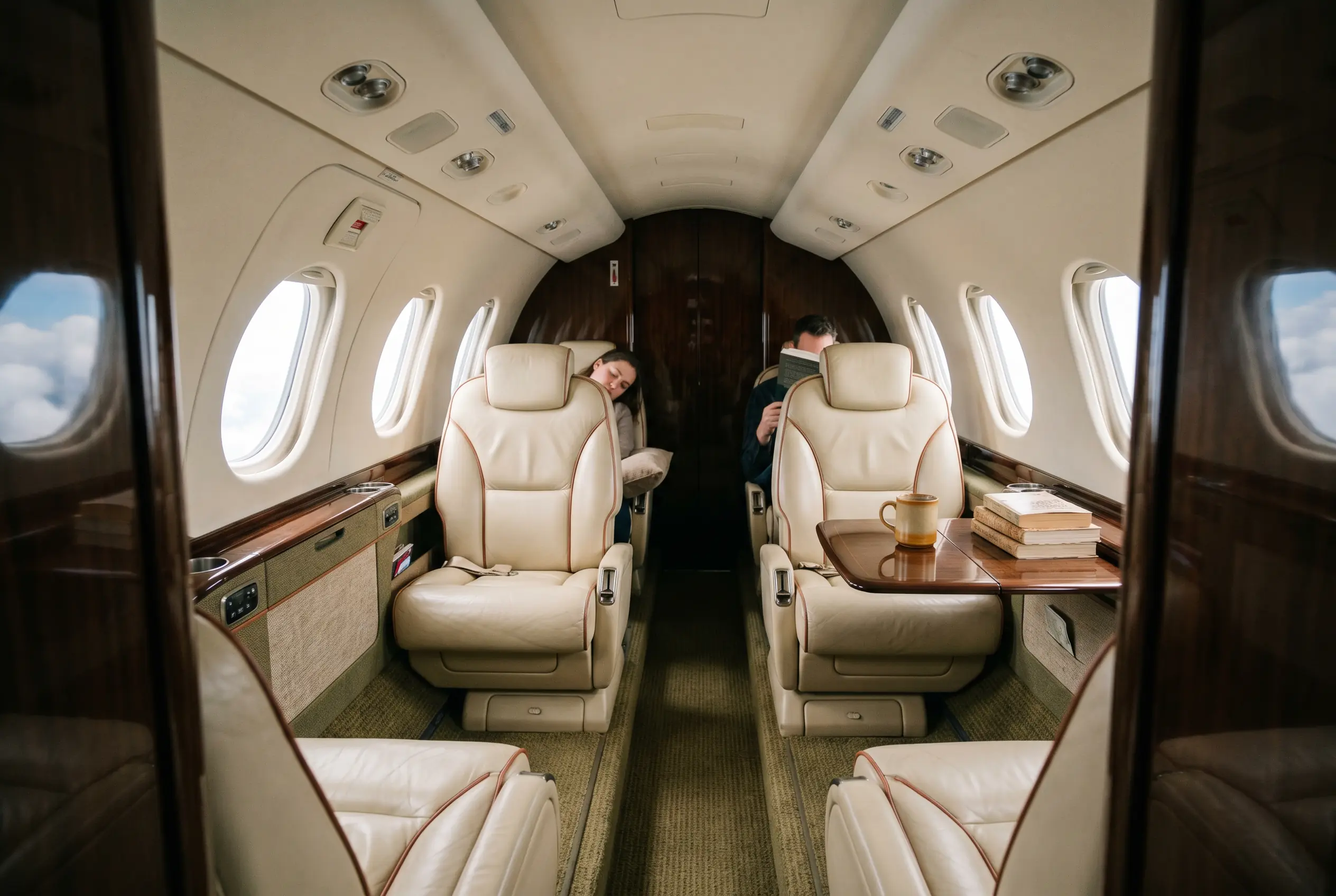 Compact jet cabin bathed in window light, four club seats in pale leather with stitched piping