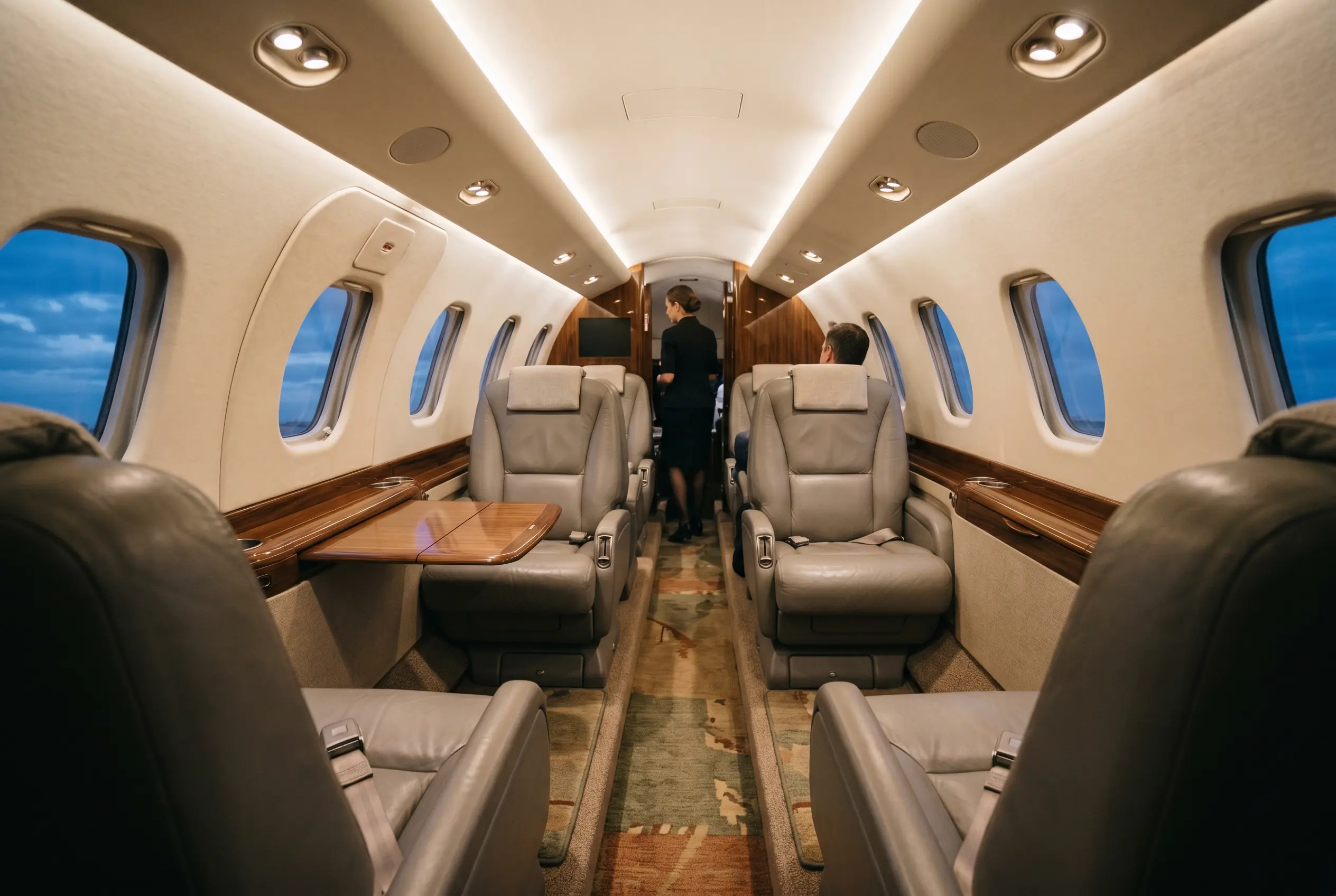 Citation XLS+ cabin at dusk, warm downwash lighting over eight stone-grey leather seats and polished veneer