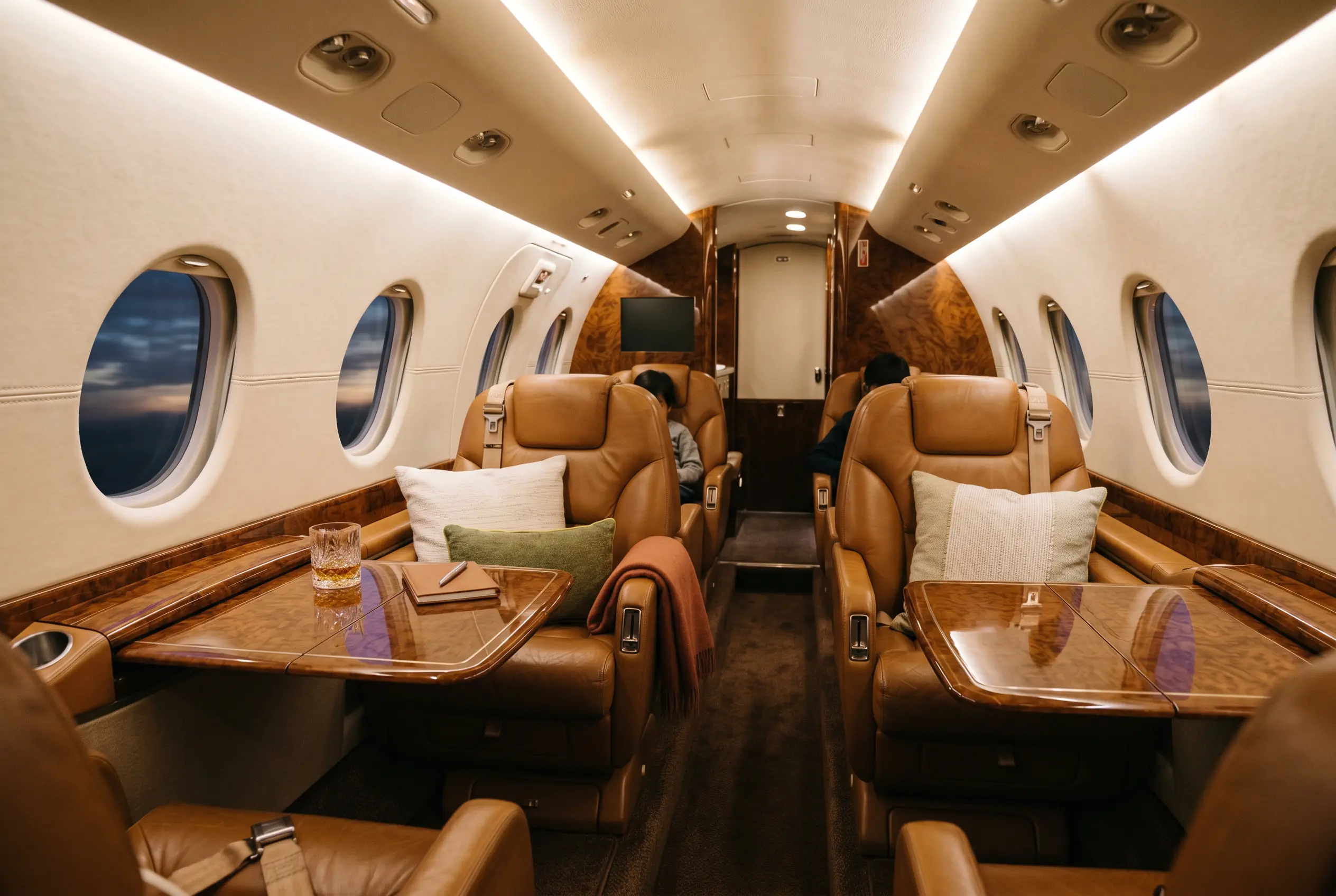 Hawker 800XP cabin glowing in low light, two facing clubs of caramel leather seats with burled wood tables deployed