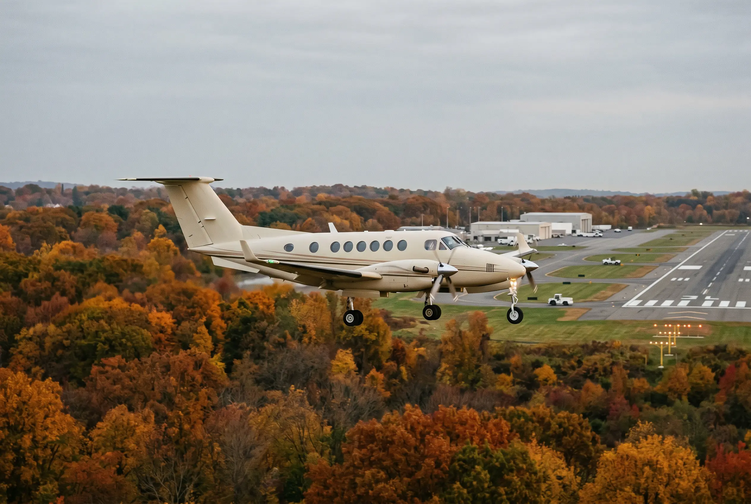 King Air 350 Large twin-engine turboprop on final approach over autumn trees, landing gear down against a soft grey sky